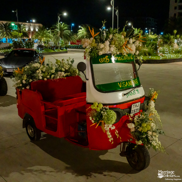 A red and white auto-rickshaw decorated elaborately with green and white fresh floral arrangements at night.