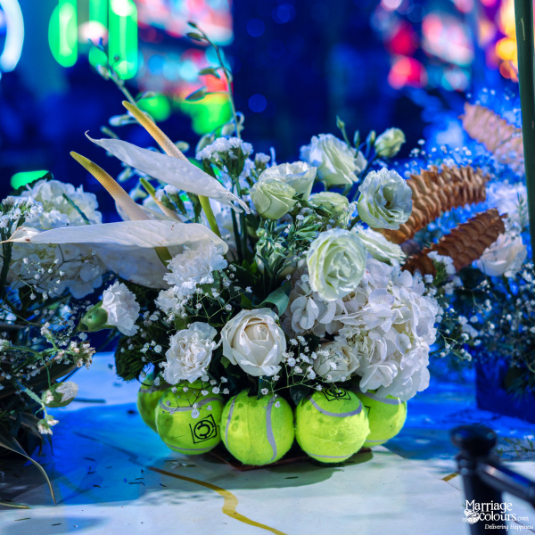 A unique floral centerpiece featuring white roses and hydrangeas resting on a base of bright green tennis balls.