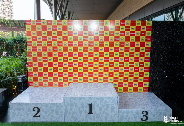 A three-tiered winner's podium with numbers 1, 2, and 3, set against a red and yellow checkered backdrop.