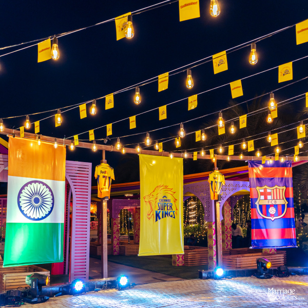 A nighttime outdoor event decorated with the Indian flag, a Chennai Super Kings banner, and an FC Barcelona flag