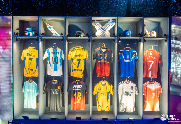 A large decorative shelving unit displaying various international soccer and cricket jerseys, bats, and helmets