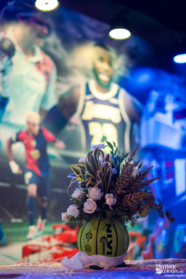 A unique floral centerpiece in a volleyball vase, set against a blurry backdrop of famous sports stars.