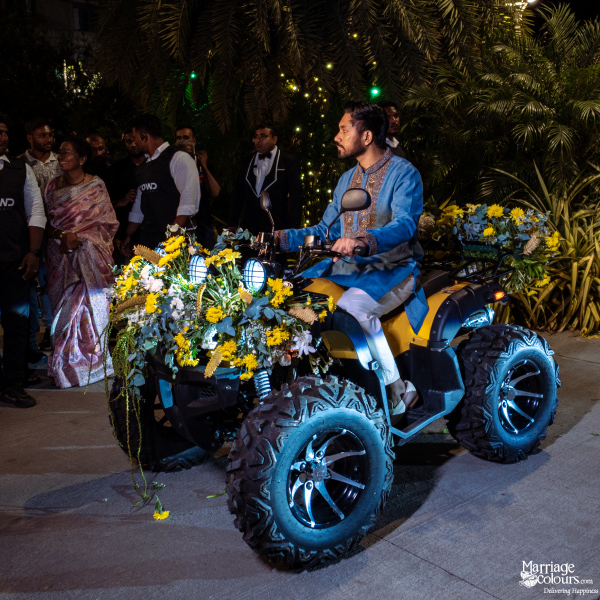 A groom riding a yellow ATV decorated with yellow flowers and green foliage for his wedding entrance.