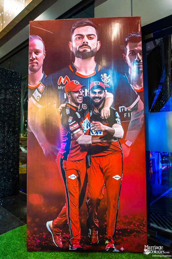 A large, vibrant banner featuring several players from the Royal Challengers Bangalore (RCB) cricket team.