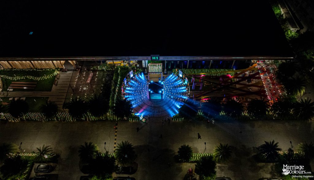 An aerial view of a large event venue at night with a brilliant, radiating blue light display.