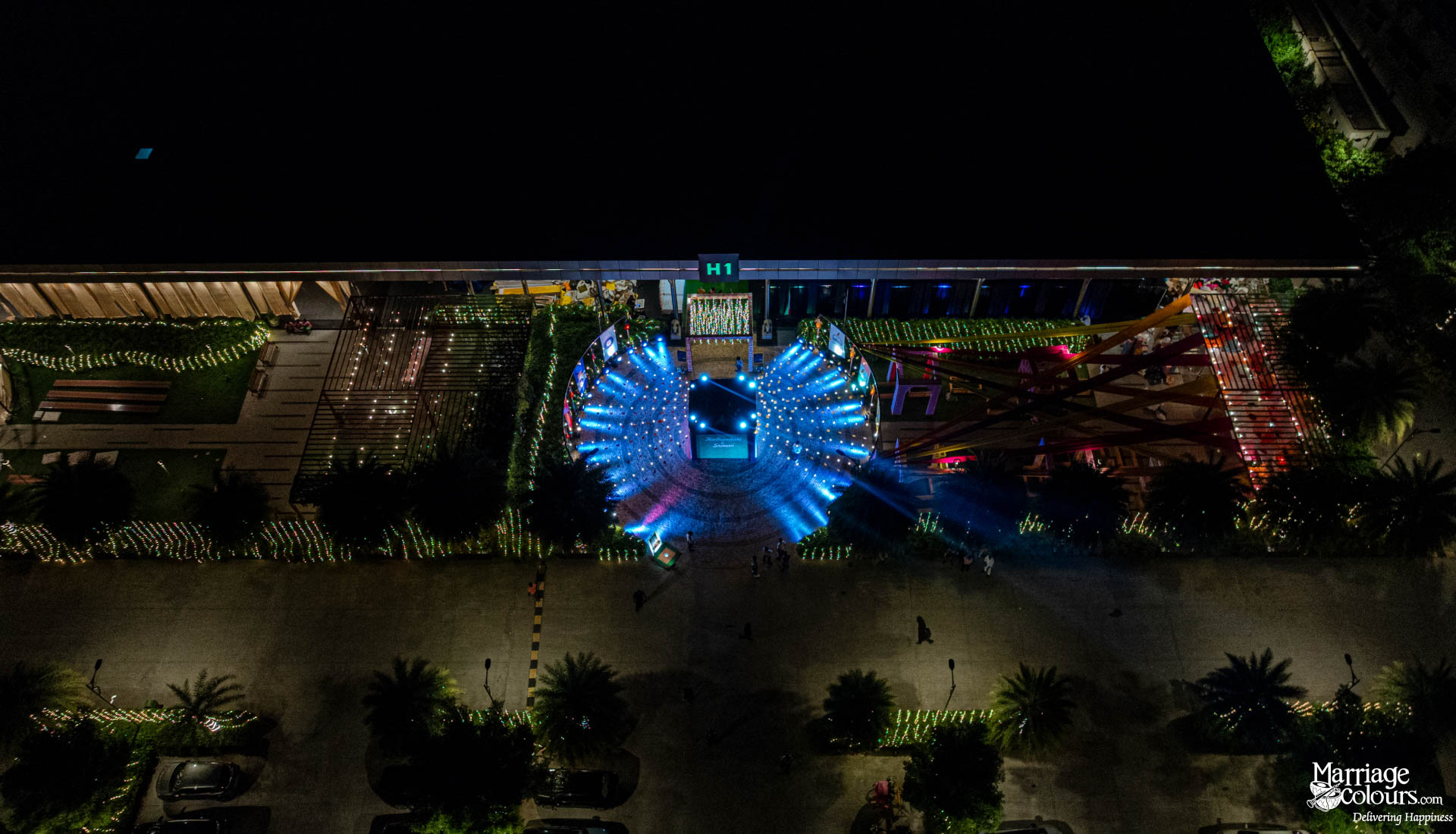 An aerial view of a large event venue at night with a brilliant, radiating blue light display.