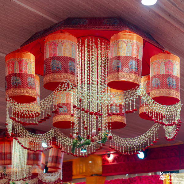 A beautiful traditional chandelier featuring orange elephant-patterned cylinders and delicate white floral bead strings.