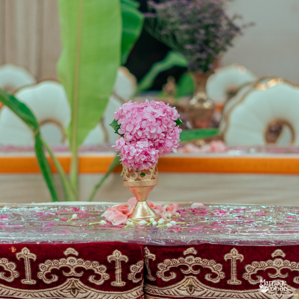 A small bouquet of pink hydrangea and rose petals in a golden vase on a plush table runner.