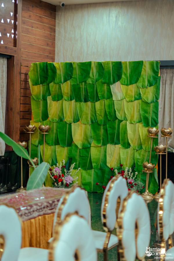 A backdrop wall covered entirely in patterned green and yellow banana leaves, framed by ornate gold lotus candle holders.