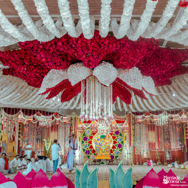 A magnificent ceremonial space with a dramatic ceiling of white and red flowers over a vibrant deity backdrop.