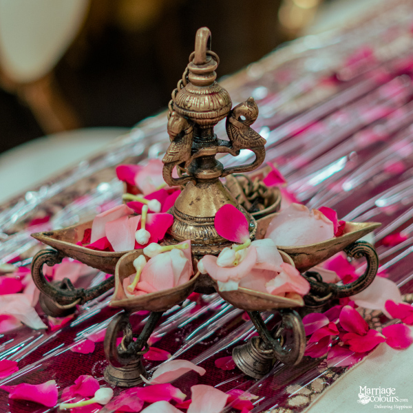 A close-up of an ornate brass oil lamp filled with pink and white rose petals and jasmine buds.
