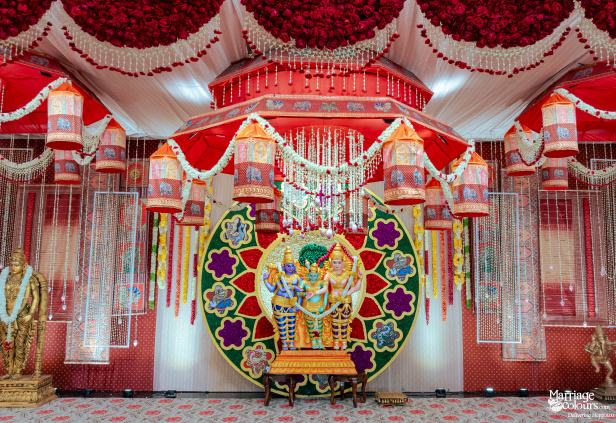 A close-up of a ceremonial stage featuring a deity statue, hanging elephant lamps, and a floral ceiling.