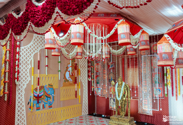 A traditional stage corner with white latticework, decorated stairs, gold statues, and elephant-patterned hanging lamps.