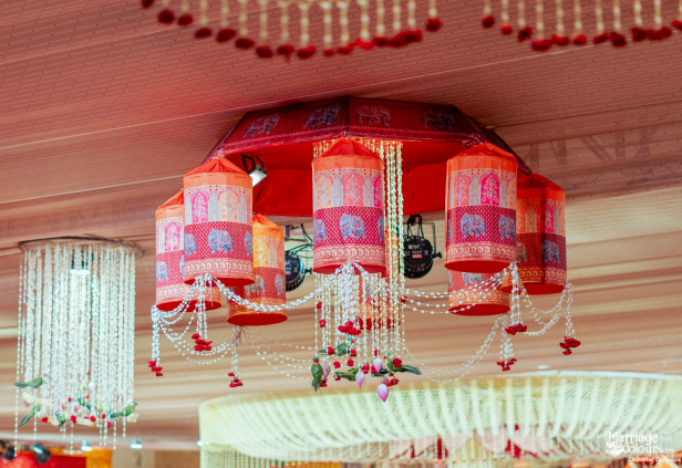 A vibrant, traditional chandelier with elephant-patterned fabric cylinders, hanging beads, and decorative miniature parrots.