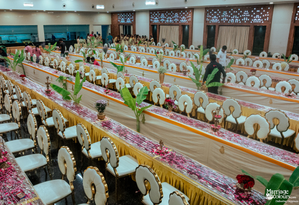 A vast, elegant dining hall with long tables, white and gold chairs, and vibrant pink and green floral runners.