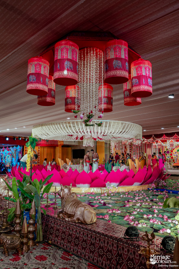 A wide-angle view of a traditional wedding mandap featuring a giant pink lotus and elephant-themed hanging lamps.