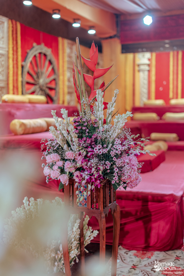 A tall, vibrant floral centerpiece with pink, white, and fuchsia flowers against a red, traditional backdrop.