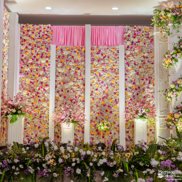 Vibrant vertical garden backdrop covered in white, pink, and yellow flowers with pink fabric draping