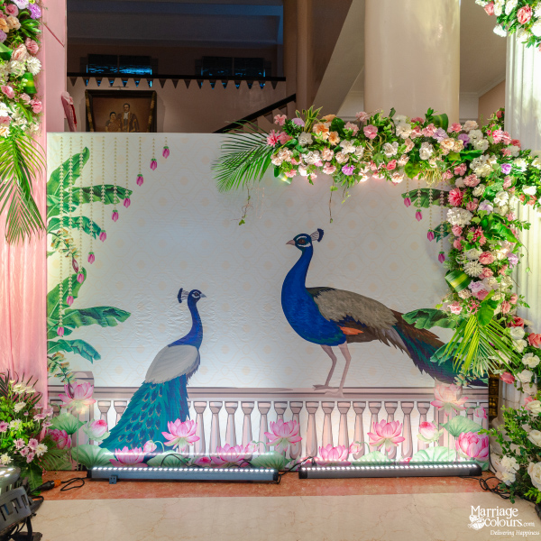 Wedding photo booth backdrop featuring painted peacocks, pink lotus flowers, and a floral arch border.