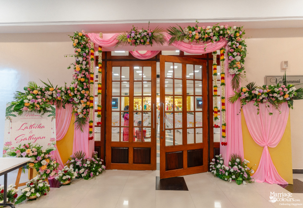 Wedding hall entrance framed by an arch of colorful flowers, pink drapes, and a welcome sign.