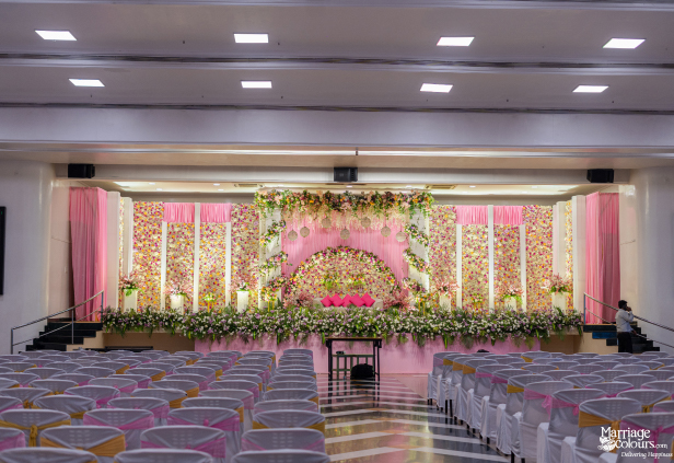 Wide view of a grand hall set up for a wedding with a pink floral stage and audience seating.