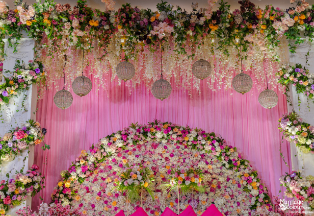 Close-up of a dreamy wedding stage with a massive floral arch, pink drapes, and hanging crystal globes.