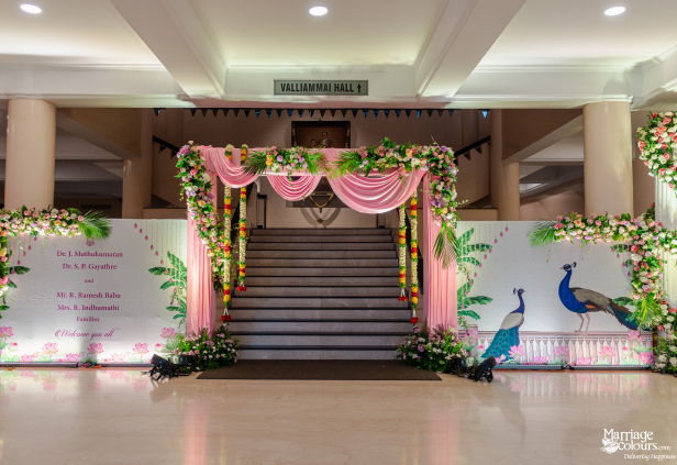 Wedding hall entrance featuring a staircase, pink draped arch, floral garlands, and peacock wall art.