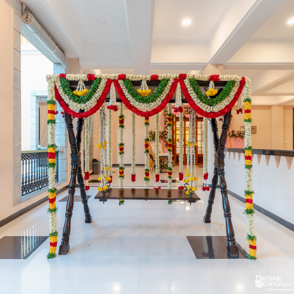 Dark wooden swing heavily decorated with traditional red, white, and yellow flower garlands for a ceremony.