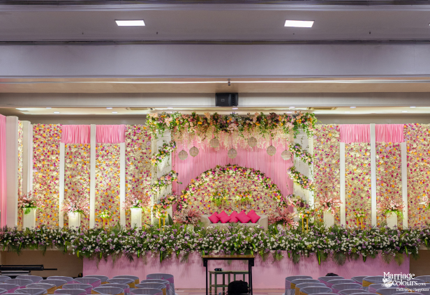 Luxurious indoor wedding stage covered completely in pink, white, and yellow flowers with pink draping.