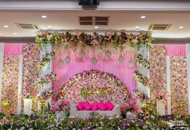 Luxurious wedding stage with a white sofa, vibrant pink flowers, and sheer pink fabric drapes.