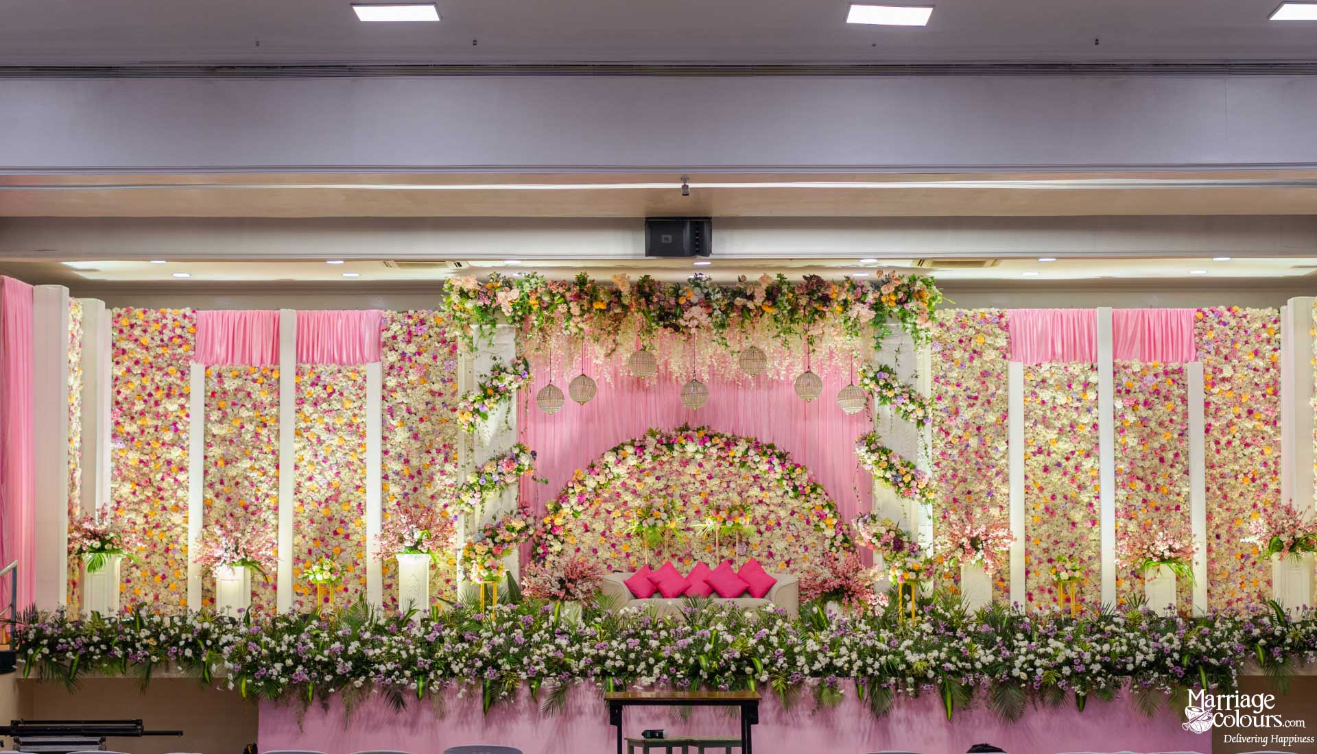 Grand indoor wedding stage fully covered in pink, white, and yellow flowers with pink draping.