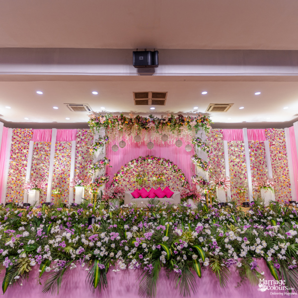 Wide view of a luxurious wedding stage featuring a floral arch, white sofa, and vibrant pink decor.