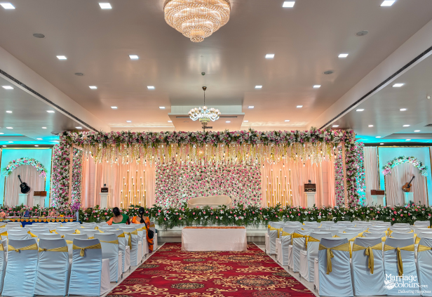 Wide view of a grand wedding hall set with chairs facing a lavish stage with pink and white flowers.