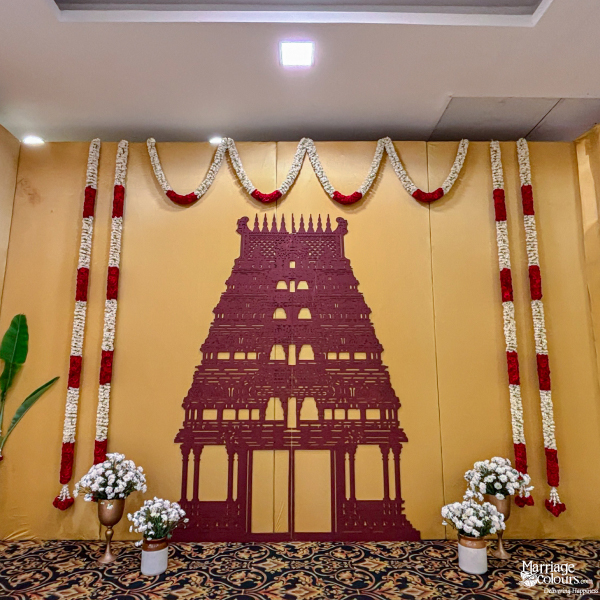 Traditional wedding backdrop with a large maroon temple tower cutout on a golden yellow wall.