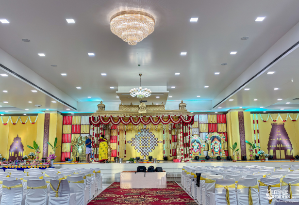 Spacious wedding hall featuring white chairs, crystal chandeliers, and a traditional red and gold stage setup.
