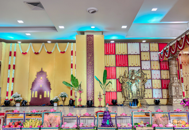 Wedding stage decor with golden deities, temple cutout, banana plants, and a colorful offering table.