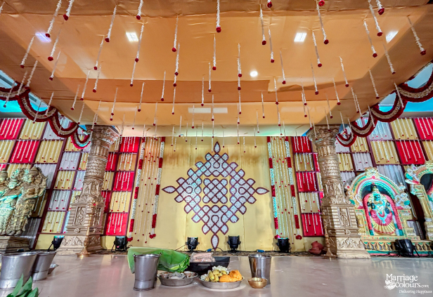 Wedding stage featuring golden pillars, a central kolam, and hanging floral strings from the canopy.