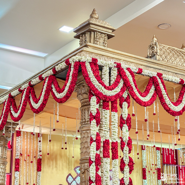 Close-up of a richly carved golden mandap pillar draped with heavy red and white flower garlands.