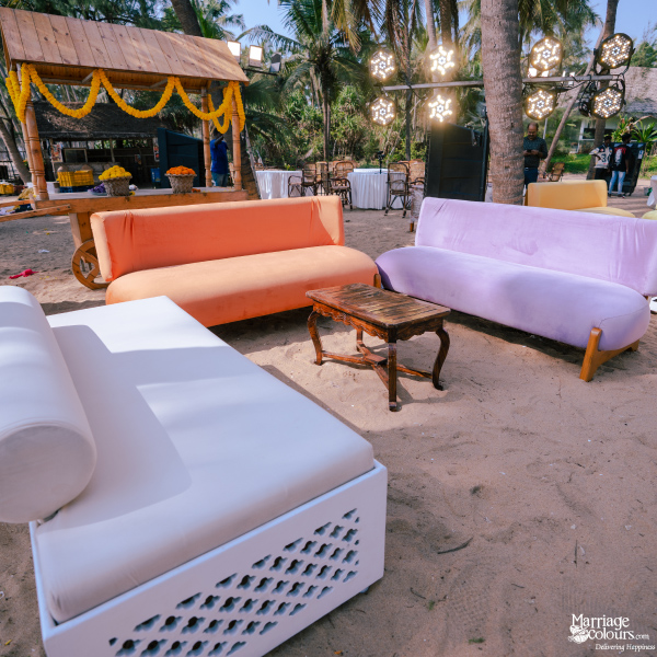 Cozy beach lounge area with colorful velvet sofas, a white daybed, and a rustic wooden table.