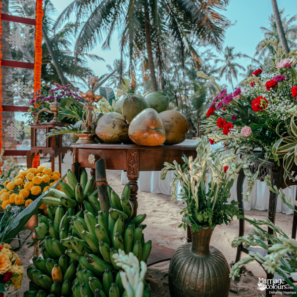 Beach event decor featuring coconuts, bananas, and flowers on a rustic wooden table by the ocean.