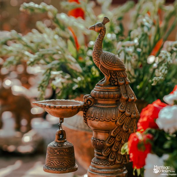 Close-up of an ornate bronze oil lamp base with a peacock figure and hanging bell.