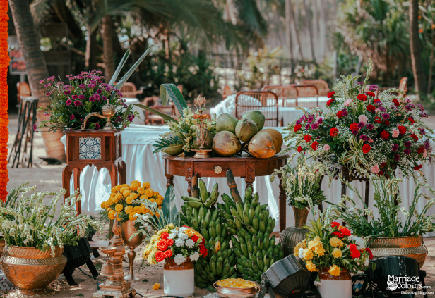 Tropical beach ceremony setup with coconuts, bananas, and vibrant flower arrangements on wooden tables.