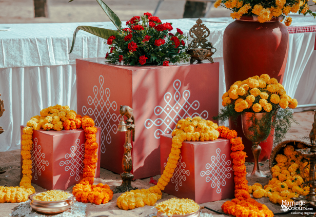 Traditional kolam art on red cubes, decorated with marigold garlands for a beach ceremony.