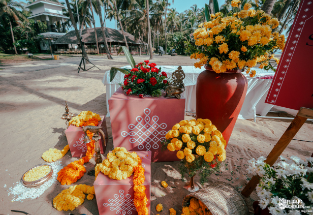 Traditional kolam designs on pink cubes, surrounded by bright yellow marigolds on the sand.