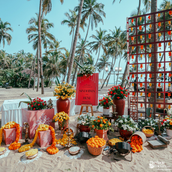 Vibrant tropical ceremony setup with marigolds, kolam boxes, and a welcome sign on the sand.