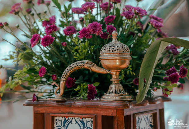 Traditional brass incense burner with a detailed handle, set among deep pink chrysanthemum flowers.