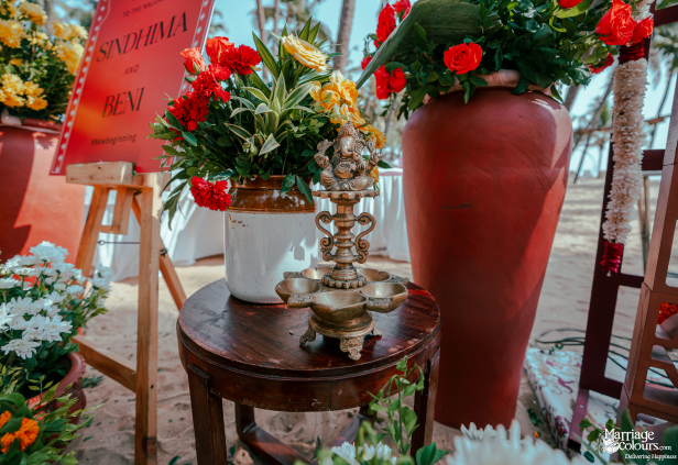Traditional brass oil lamp featuring a deity, surrounded by colorful flowers on a small wooden table.
