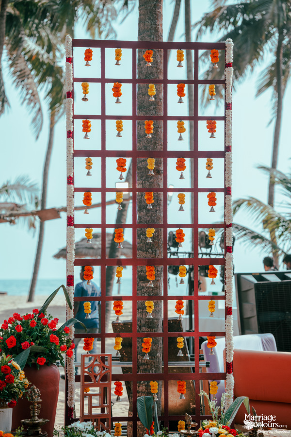 Beach wedding lattice decorated with hanging orange and yellow marigold flower strings.