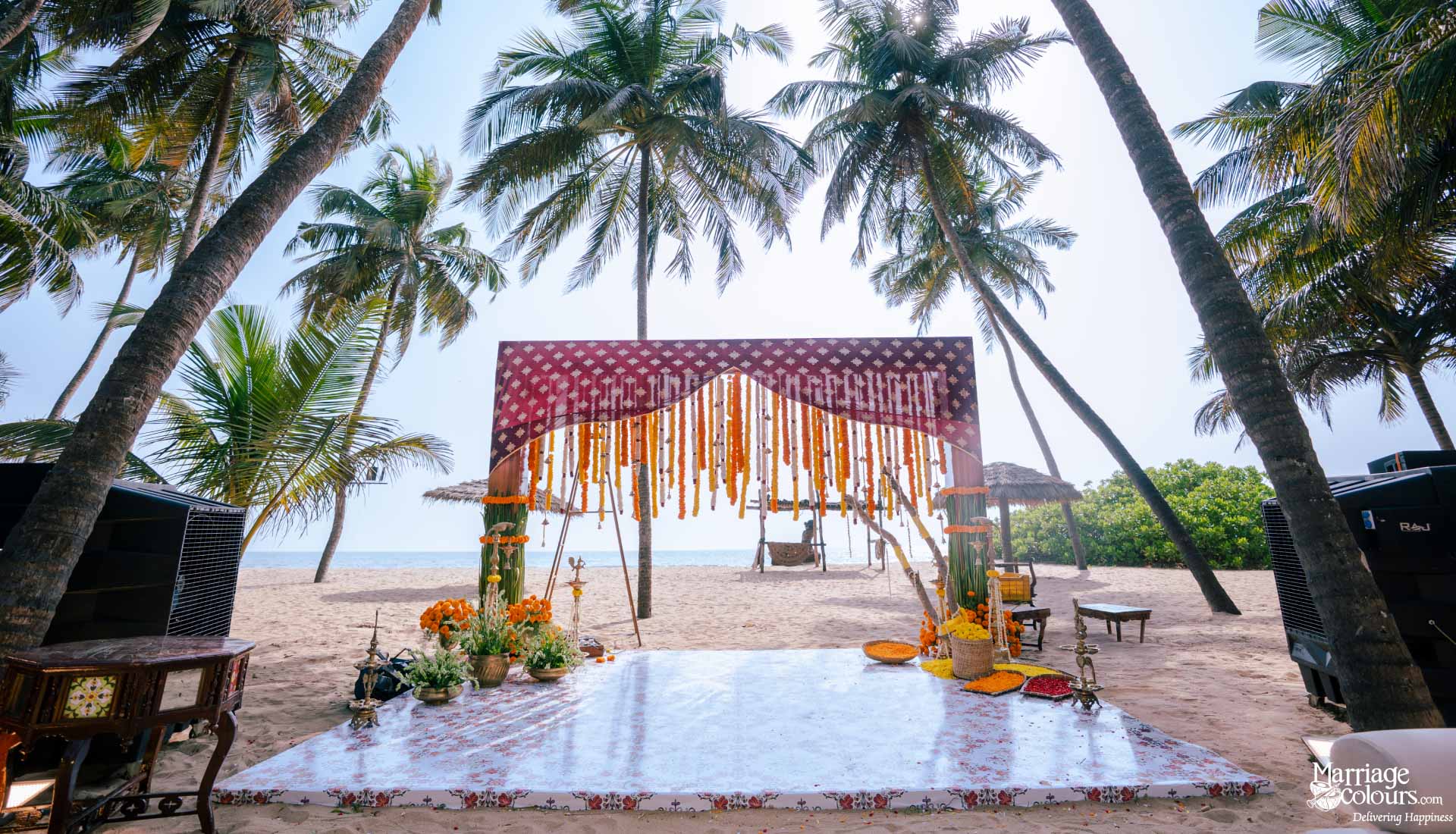 Scenic beach wedding mandap with palm trees, a marigold curtain, and a clear dance floor.