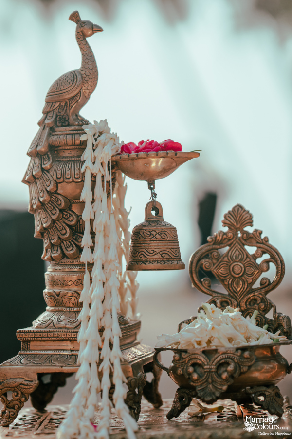 Ornate bronze peacock statue with a hanging bell and bowl of rose petals for a ceremony.